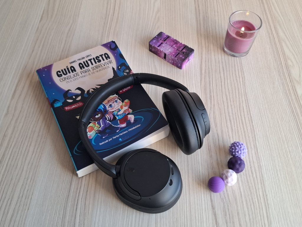 Materiales de apoyo para personas autistas con libro, cascos de cancelación de sonido y fidget toys en un espacio terapéutico